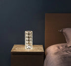 Crystal glass with geometric pattern on wooden bedside table next to bed with mauve sheets