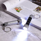 Compact metal LED keychain flashlights in silver and black on marble surface beside open book