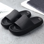 Pair of black textured foam slide sandals on gray surface with folded towels in background