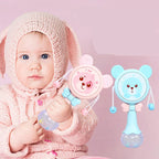 Baby in pink knit hoodie holding blue and pink bear-shaped baby rattles with round handles