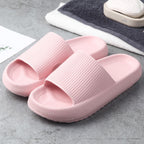 Pair of light pink textured slip-on sandals on gray surface with towels and soap in background