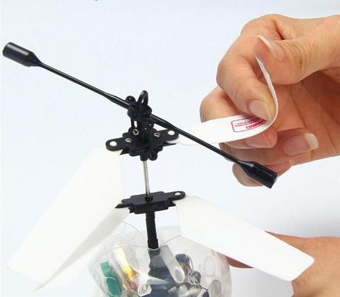Hand peeling off protective film from rotor blade of small remote control helicopter
