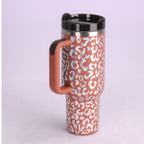 Insulated travel mug with orange and white leopard print design and black lid on light purple background