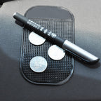 Black anti-slip pad holding black and silver pen with Chinese writing and three silver coins on a dark textured surface