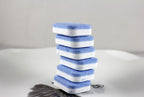 Stack of six blue and white dishwasher detergent tablets on a white surface with a feather design