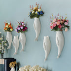 White ceramic fish-shaped wall vases with colorful artificial flowers on blue wall