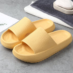 Pair of yellow textured foam slide sandals on gray floor with towels and soap nearby