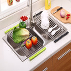 Roll-up dish drying racks with green and black silicone edges over dual stainless steel kitchen sink holding fresh vegetables, bowls, and spoons