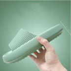 Hand holding a mint green textured slip-on sandal with a thick sole against a green background